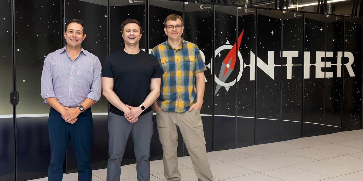 Three men smiling together in front of an exascale supercomputer